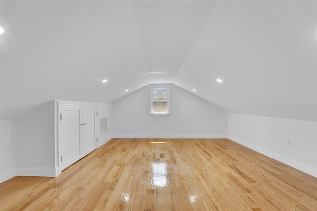 additional living space with light wood finished floors, visible vents, baseboards, and lofted ceiling