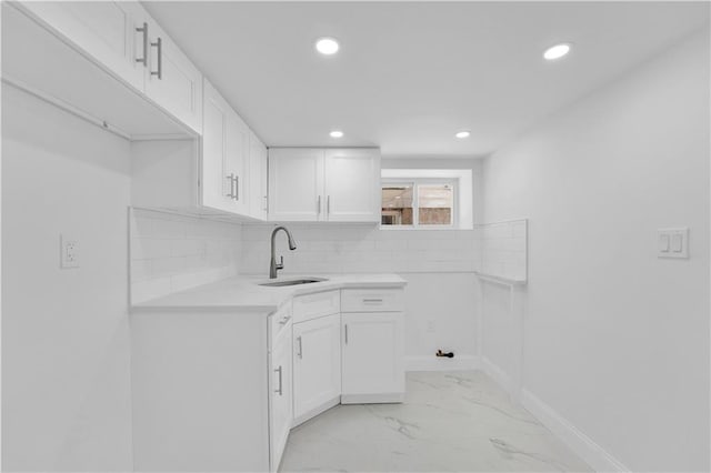 kitchen featuring backsplash, light countertops, white cabinets, marble finish floor, and a sink