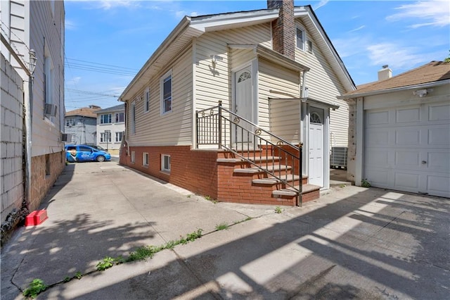 view of front facade with cooling unit, a chimney, a garage, aphalt driveway, and brick siding