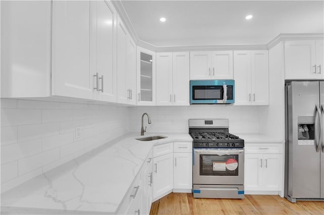 kitchen featuring light wood-style flooring, a sink, stainless steel appliances, white cabinets, and light stone countertops