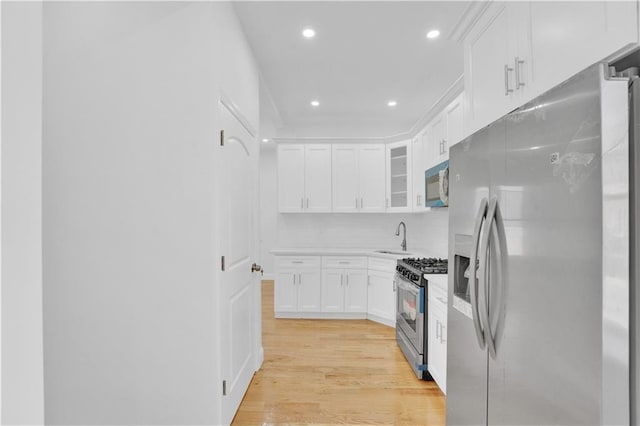 kitchen with a sink, white cabinetry, stainless steel appliances, light wood finished floors, and light countertops