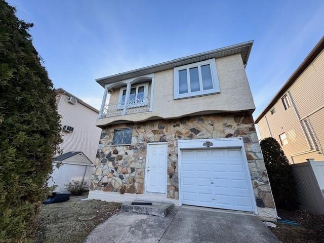 front facade with a garage, fence, stone siding, driveway, and stucco siding