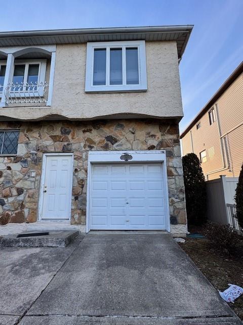 exterior space featuring stucco siding, concrete driveway, fence, a garage, and stone siding