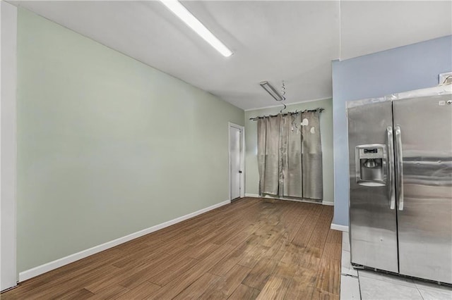 kitchen featuring baseboards, wood finished floors, and stainless steel refrigerator with ice dispenser