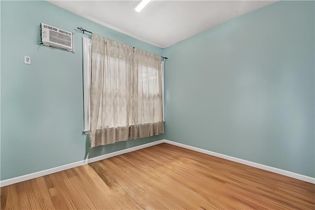 spare room with baseboards, an AC wall unit, and wood finished floors