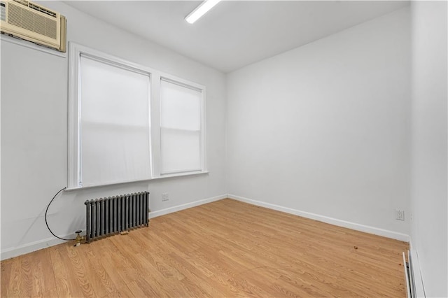 spare room featuring baseboards, radiator heating unit, a wall unit AC, wood finished floors, and a baseboard radiator