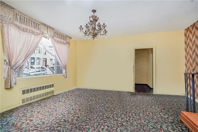 carpeted empty room featuring a notable chandelier, radiator heating unit, and baseboards