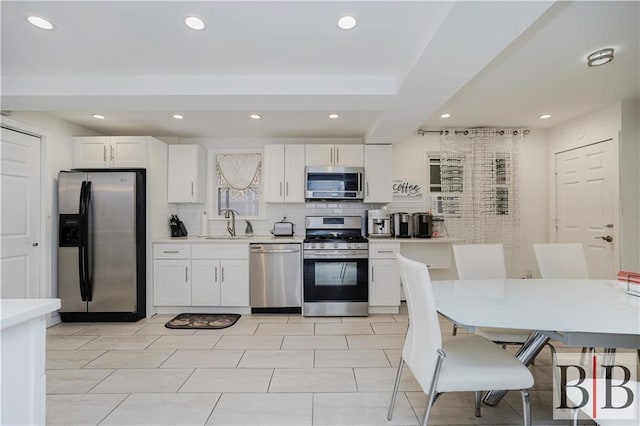 kitchen with light countertops, decorative backsplash, stainless steel appliances, white cabinetry, and a sink