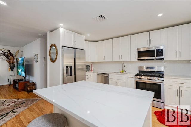 kitchen featuring visible vents, decorative backsplash, light wood-style flooring, stainless steel appliances, and a sink