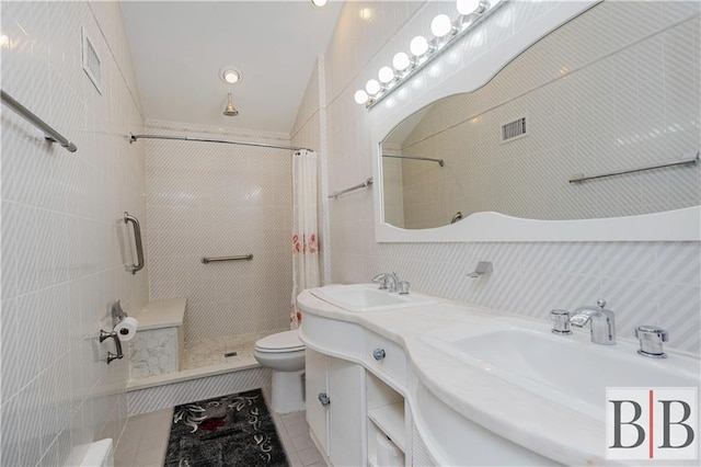 full bathroom with visible vents, toilet, a tile shower, tile walls, and a sink