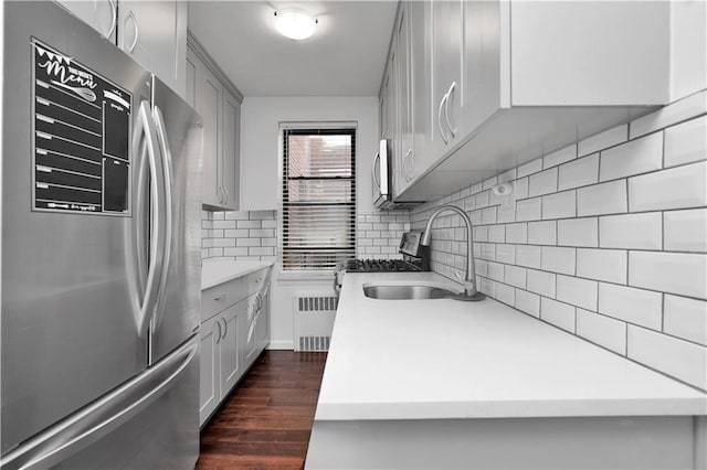 kitchen featuring dark wood finished floors, backsplash, radiator heating unit, appliances with stainless steel finishes, and a sink