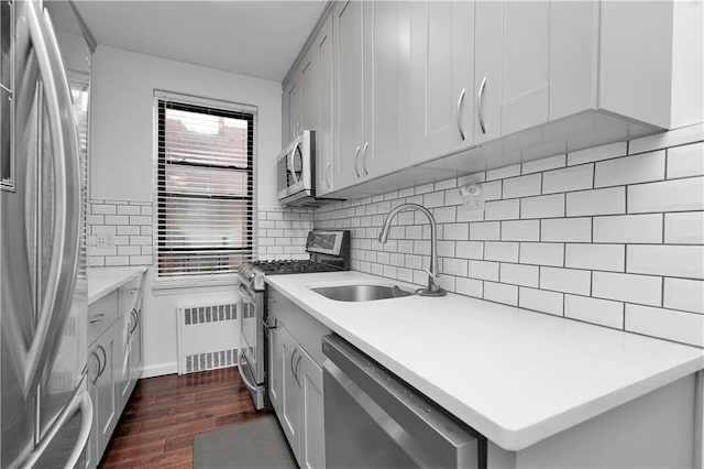 kitchen with tasteful backsplash, dark wood-style floors, radiator heating unit, stainless steel appliances, and a sink