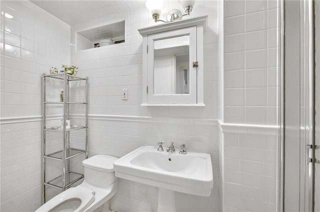 bathroom with a sink, toilet, and tile walls