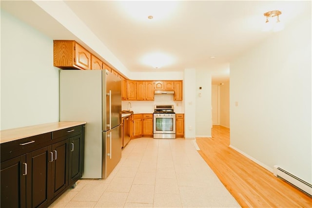 kitchen featuring under cabinet range hood, a baseboard heating unit, appliances with stainless steel finishes, light countertops, and baseboards