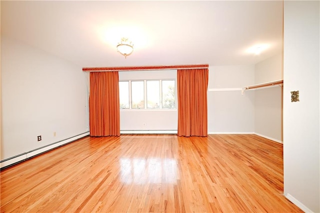 spare room with baseboard heating, a baseboard heating unit, baseboards, and wood finished floors