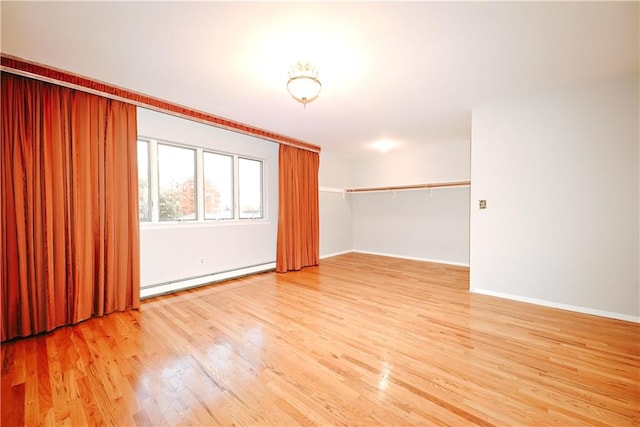 spare room with a baseboard heating unit, baseboards, and wood finished floors