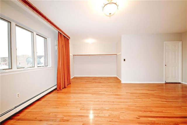 unfurnished room featuring baseboard heating, light wood-type flooring, and baseboards