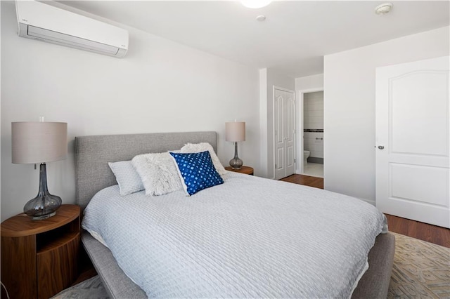 bedroom featuring connected bathroom, an AC wall unit, and wood finished floors