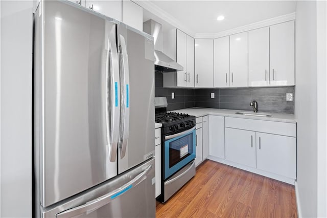 kitchen with wall chimney range hood, light wood-type flooring, light countertops, appliances with stainless steel finishes, and a sink