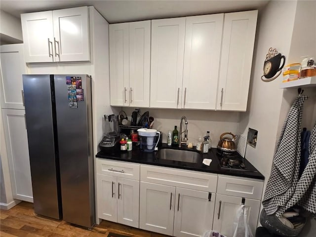 kitchen with white cabinetry, dark countertops, freestanding refrigerator, and a sink