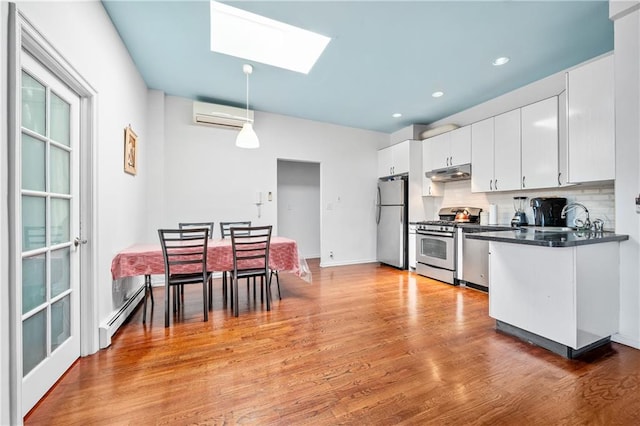 kitchen with dark countertops, under cabinet range hood, an AC wall unit, baseboard heating, and stainless steel appliances