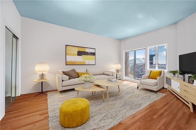 living room with a baseboard heating unit, baseboards, and light wood-type flooring