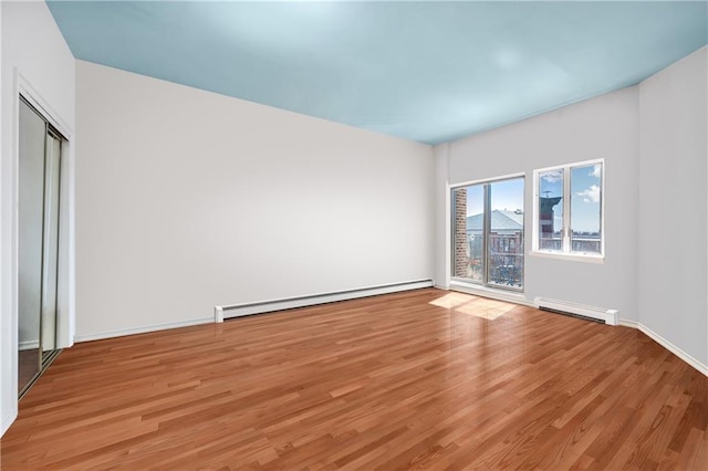 empty room featuring a baseboard heating unit, light wood-style flooring, and baseboards