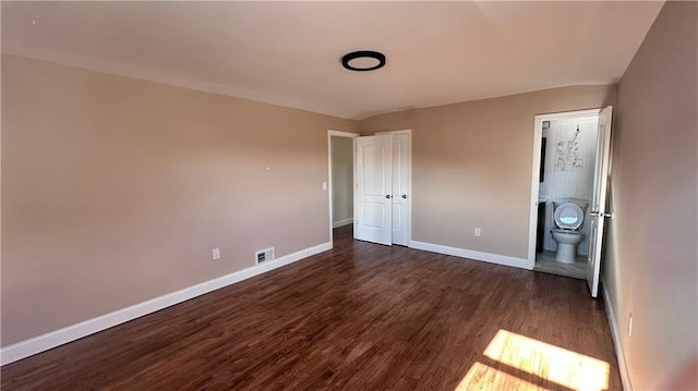 unfurnished bedroom with visible vents, baseboards, dark wood-type flooring, and ensuite bath