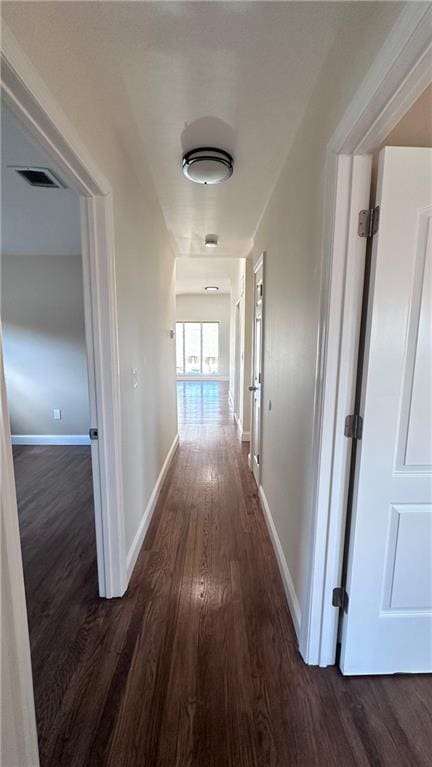 hallway featuring baseboards, visible vents, and dark wood-style flooring