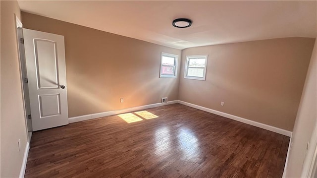 empty room featuring dark wood-type flooring, visible vents, and baseboards