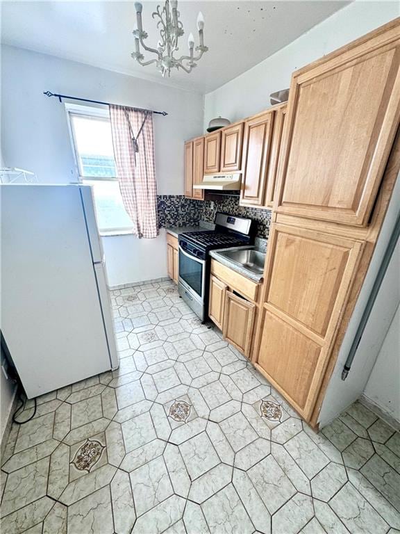 kitchen with backsplash, under cabinet range hood, freestanding refrigerator, an inviting chandelier, and stainless steel gas stove