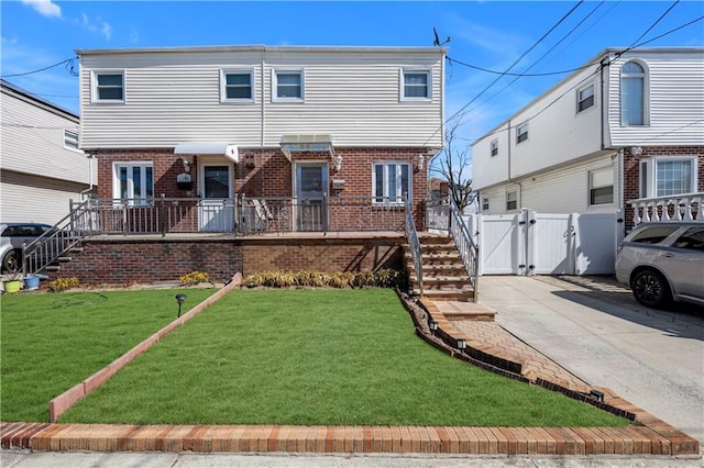 view of front of home with brick siding, a front lawn, fence, driveway, and a gate