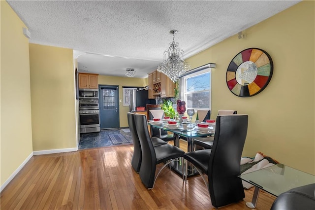 dining space featuring a chandelier, a textured ceiling, baseboards, and hardwood / wood-style floors