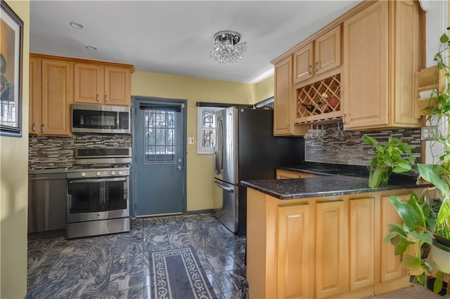 kitchen with backsplash, appliances with stainless steel finishes, dark stone counters, and a peninsula