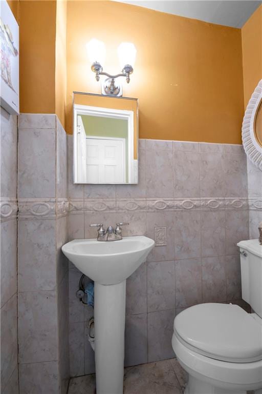 half bathroom featuring wainscoting, toilet, and tile walls