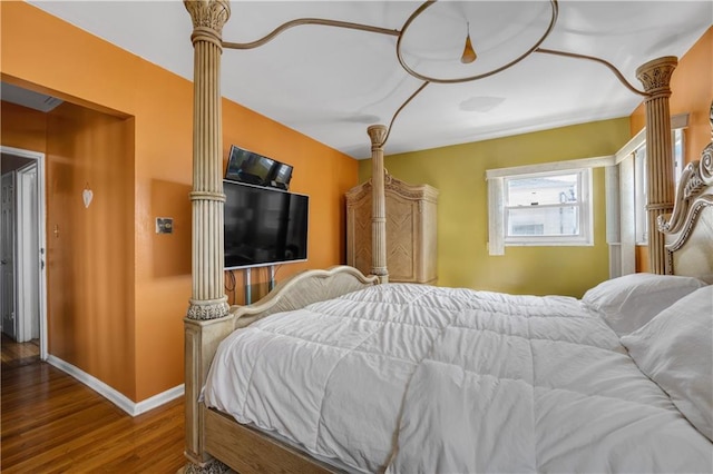 bedroom featuring wood finished floors, baseboards, and decorative columns