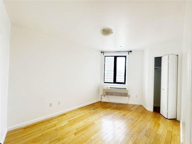 unfurnished bedroom with baseboards, light wood finished floors, and a wall mounted AC