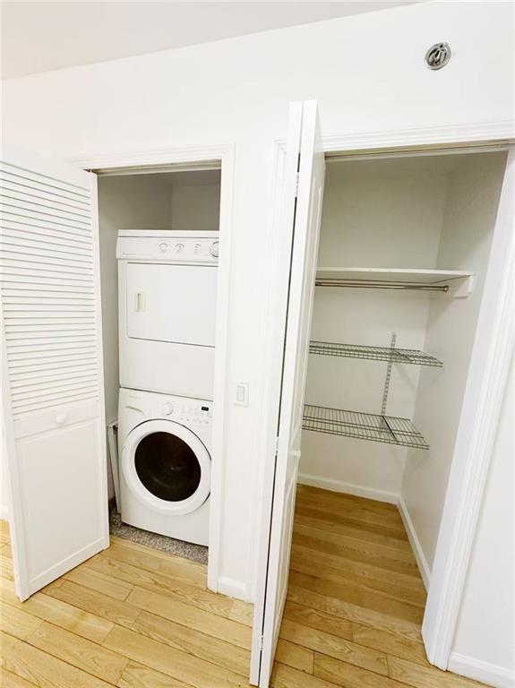 clothes washing area featuring laundry area, light wood-type flooring, baseboards, and stacked washer and dryer