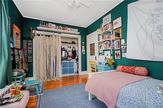 bedroom with a ceiling fan, crown molding, wood finished floors, and a closet