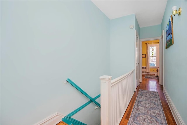 hall with an upstairs landing, baseboards, and wood-type flooring