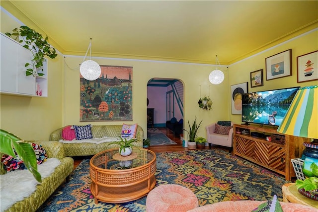 living area featuring arched walkways, wood finished floors, and ornamental molding