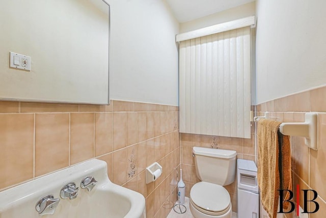 bathroom with tile walls, toilet, wainscoting, and a sink