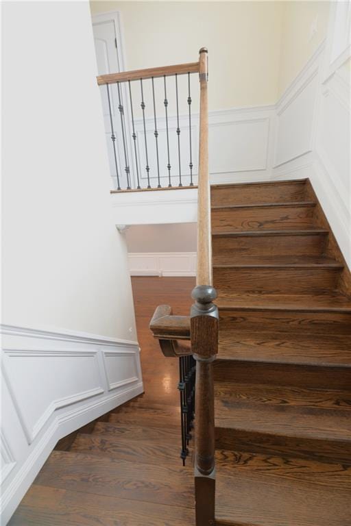 stairs featuring a decorative wall, wood finished floors, and a wainscoted wall