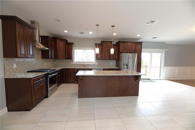 kitchen with a wainscoted wall, visible vents, appliances with stainless steel finishes, wall chimney exhaust hood, and a center island