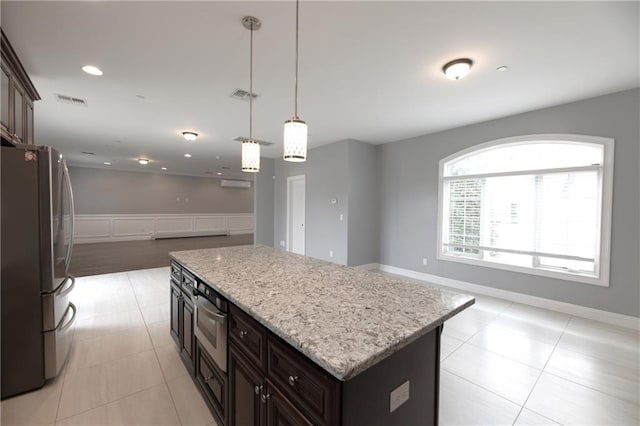 kitchen with freestanding refrigerator, a kitchen island, a wainscoted wall, open floor plan, and light stone counters