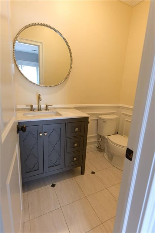 bathroom with tile patterned floors, toilet, wainscoting, a decorative wall, and vanity