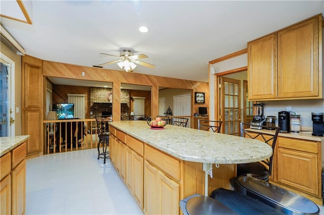 kitchen featuring a ceiling fan, wooden walls, a breakfast bar area, a fireplace, and light stone countertops