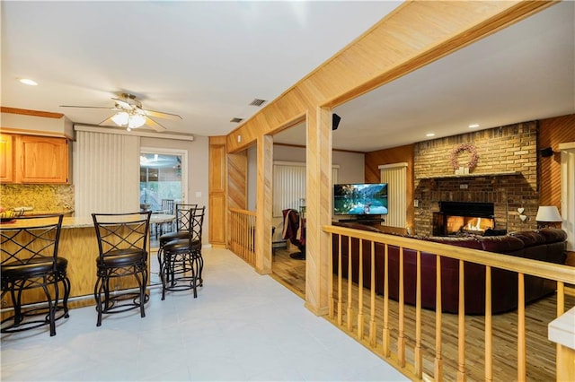 interior space featuring open floor plan, a breakfast bar area, a peninsula, a fireplace, and a ceiling fan