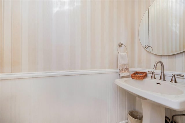 bathroom featuring a sink, a wainscoted wall, and wallpapered walls