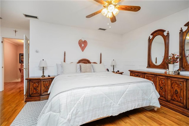 bedroom featuring light wood-type flooring, visible vents, ceiling fan, and wainscoting